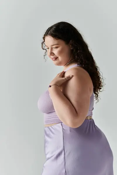 Uma mulher plus size sorri suavemente em uma roupa de lavanda contra um fundo neutro. — Fotografia de Stock