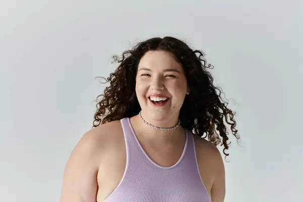 Веселая женщина plus size с кудрявыми волосами сияет в стильной, серенькой обстановке. — стоковое фото