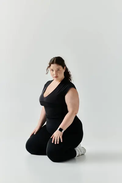 A beautiful plus size woman dressed in black kneels gracefully, exuding confidence and elegance. — Stock Photo