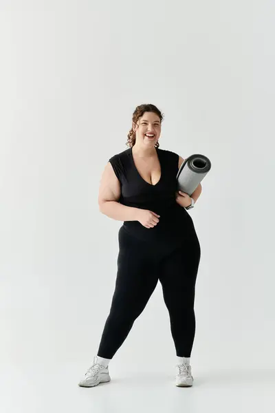 The beautiful plus size woman stands confidently with a yoga mat, embracing her wellness routine. — Stock Photo