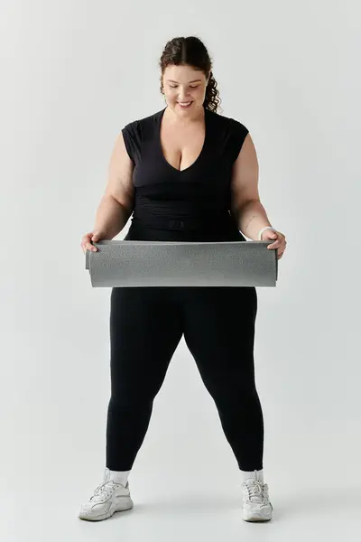 Una elegante mujer de talla grande sostiene una esterilla de yoga, lista para abrazar una práctica calmante. - foto de stock
