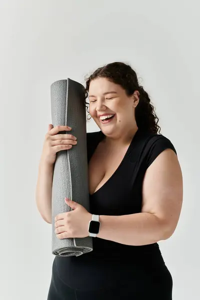 A cheerful plus size woman holds her yoga mat, radiating happiness in a tranquil environment. — Stock Photo