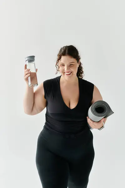 Eine selbstbewusste, schöne Frau hält eine Wasserflasche und eine Yogamatte in der Hand und freut sich auf ihre Trainingsreise. — Stockfoto