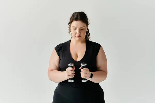 Uma mulher bonita plus size concentra-se em seu treino enquanto segurando halteres dentro de casa. — Fotografia de Stock