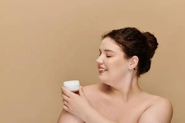 Una elegante mujer de talla grande disfruta de su ritual de cuidado de la piel con una sonrisa en un ambiente relajante. - foto de stock