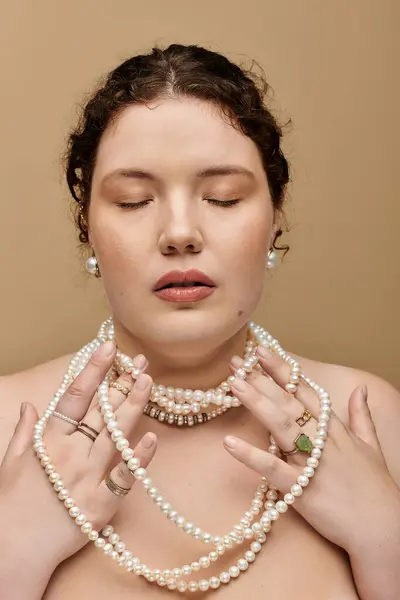 A beautiful plus size woman gently embraces strands of pearls, radiating elegance and confidence. — Stock Photo