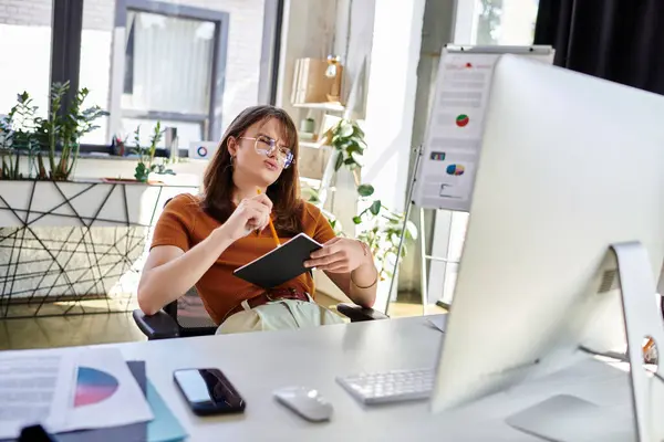 A young non binary individual thoughtfully reflects while surrounded by greenery and office tools. — Stock Photo