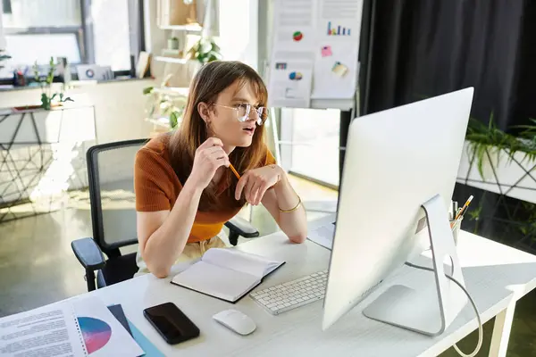 The young non binary individual engages with a computer, pondering over tasks in a bright office. — Stock Photo