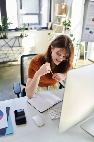 In a contemporary office, a young non binary individual smiles while working diligently on tasks. — Stock Photo