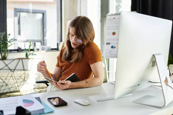 A young non binary person diligently writes notes while working at a modern office desk. — Stock Photo