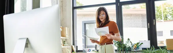 In a bright office, a young non binary individual examines documents, surrounded by greenery. — Stock Photo