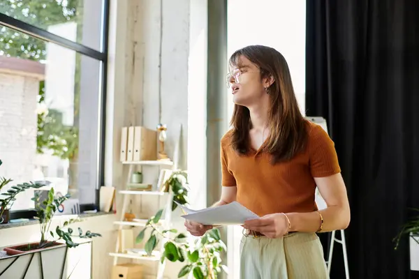 In einem modernen Büro präsentiert eine junge nichtbinäre Person aufgeregt Materialien inmitten von Grün. — Stockfoto