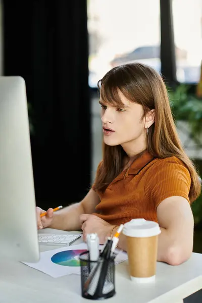 Um jovem não binário focado trabalha em um computador em um escritório elegante. — Fotografia de Stock