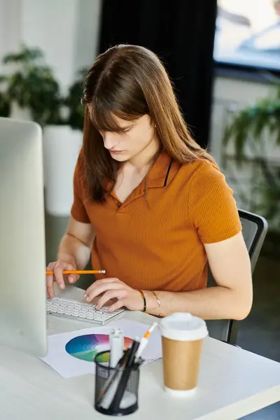 Un giovane individuo non binario si concentra sul proprio lavoro su una scrivania in un ufficio moderno. — Foto stock