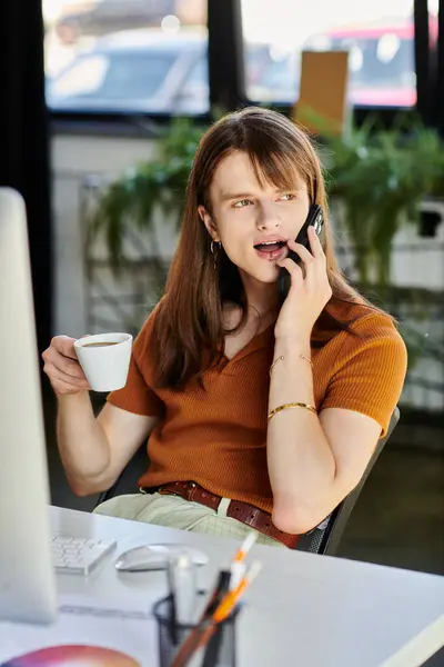 Una persona no binaria habla por teléfono mientras disfruta del café en un ambiente de trabajo vibrante. — Stock Photo