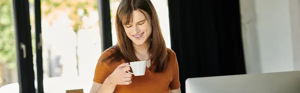 A non binary person smiles with coffee in a bright, stylish workspace. — Stock Photo