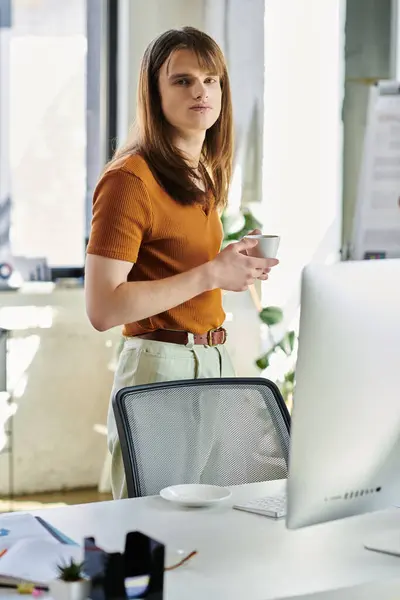 In a sunlit office, a non binary individual stands thoughtfully with a cup in hand, contemplating. — Stock Photo