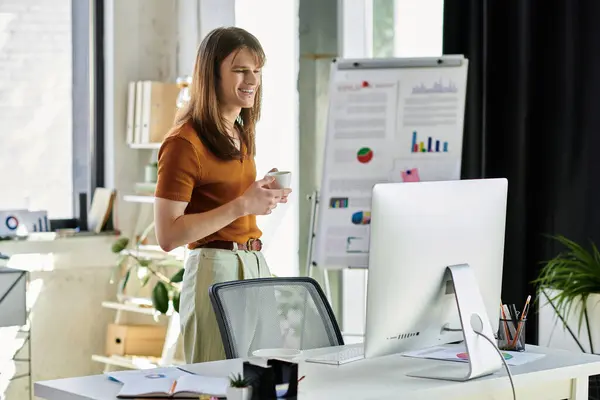 A young non binary individual stands smiling with a phone, surrounded by office materials. — Stock Photo