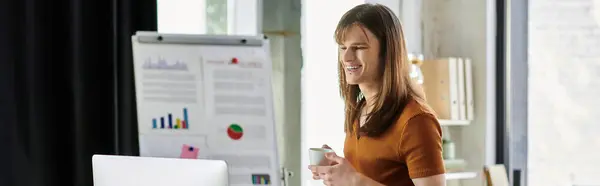 Smiling non binary individual discusses ideas while holding a cup in a vibrant workspace. — Stock Photo