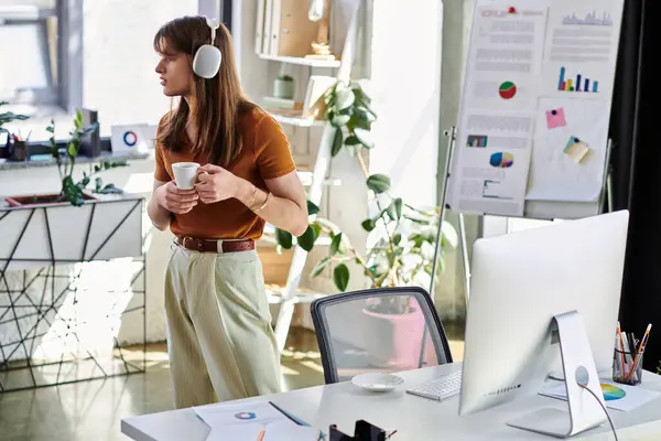 In a bright office, a young non binary person enjoys coffee and music with headphones. — Stock Photo