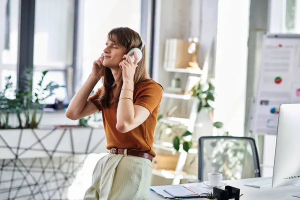 Engagé dans un moment de joie, un jeune non binaire écoute de la musique dans un lieu de travail animé. — Photo de stock