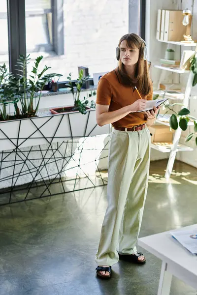 Engaged in a task, the young non binary individual stands in a vibrant office filled with greenery. — Stock Photo