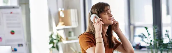 A young non binary individual listens to music with a smile in a modern office environment. — Stock Photo
