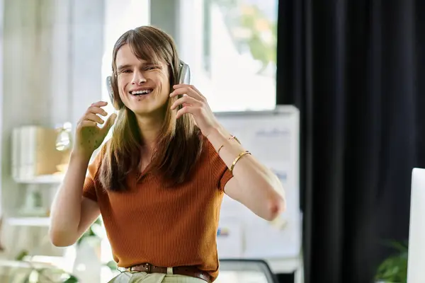 Un alegre joven no binario individuo usando auriculares y sonriendo en un espacio de trabajo creativo. — Stock Photo
