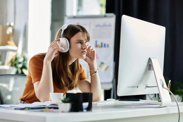 Concentrating on a computer screen, a young non binary person listens attentively while working. — Stock Photo