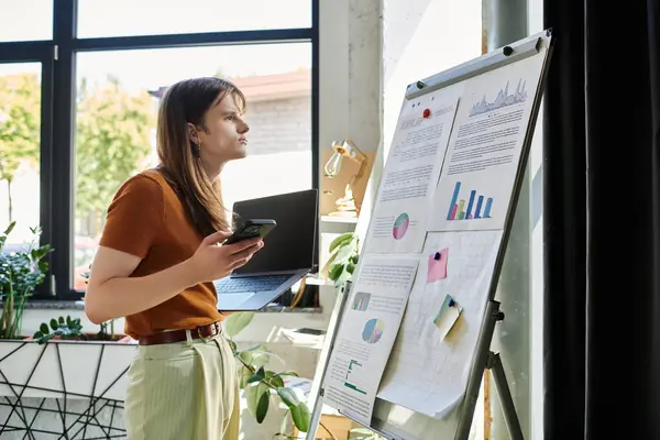 A focused young non binary individual analyzes data presentations in a modern office. — Stock Photo