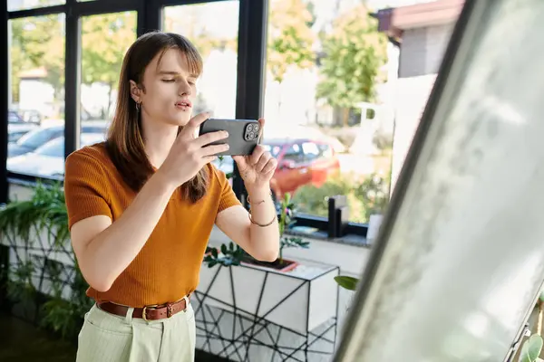 A young non binary person thoughtfully examines their smartphone in a modern office. — Stock Photo