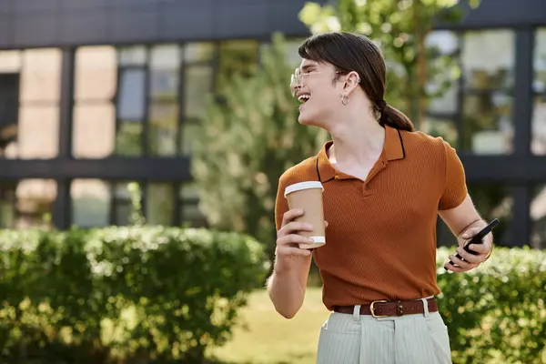 A person smiles brightly while holding coffee and a phone in a vibrant outdoor office setting. — Stock Photo