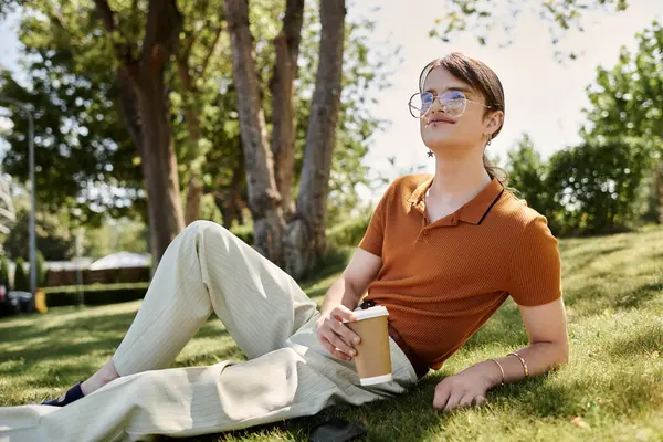 Una persona no binaria se relaja con café en un jardín de oficinas soleado y colorido. - foto de stock