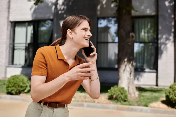 A young non binary person is happily talking on the phone, enjoying the sunny day outside. — Stock Photo