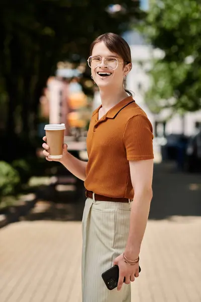 The young non binary person smiles brightly with a coffee in hand, soaking in the lively atmosphere. — Stock Photo
