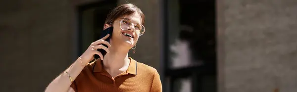 A non binary individual engages in a lively conversation on their phone in a bright office. — Stock Photo
