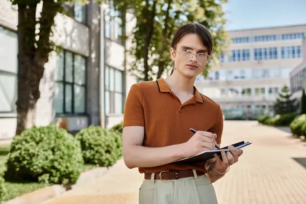 Un individuo no binario se para al aire libre, tomando notas en un portapapeles mientras absorbe la luz del sol. - foto de stock