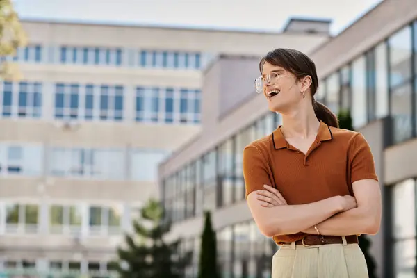 Standing confidently in the sunlight, a young non binary individual smiles outside their workplace. — Stock Photo