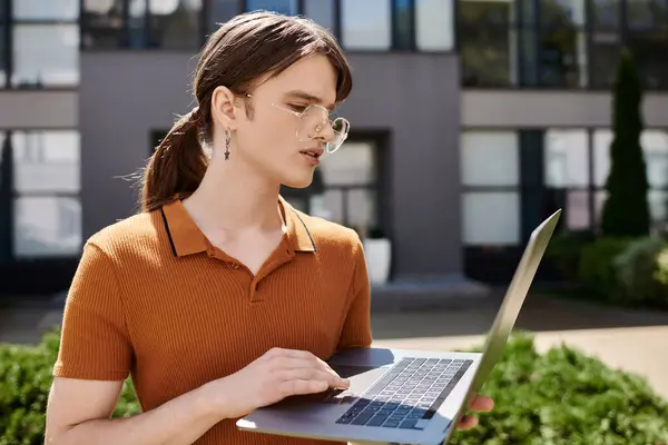 A young non binary person is focused on their laptop outside a contemporary office building. — Stock Photo