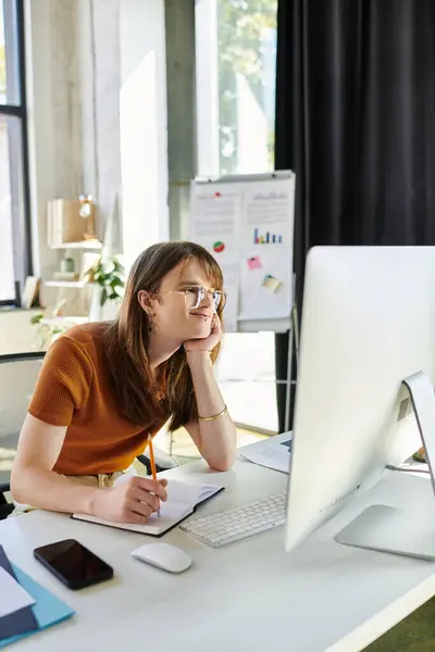 A young non binary person is deep in thought while working at a desk in an inviting office space. — Stock Photo