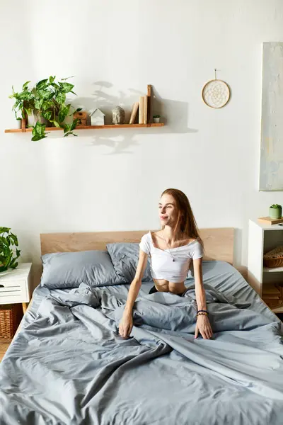 A young woman sits on her unmade bed, surrounded by soft blankets, reflecting quietly in her peaceful room. — Stock Photo