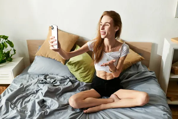 A young woman sits on her bed, smiling as she having video call in her cozy room. — Stock Photo