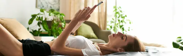A young woman navigates her daily life with anorexia, resting on her bed and using her phone surrounded by plants. — Stock Photo