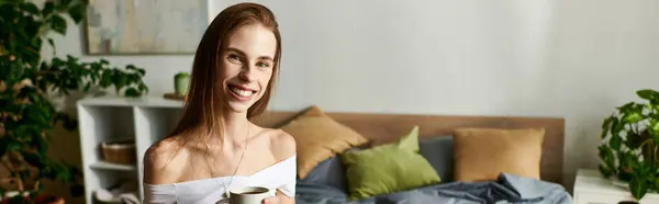 Smiling and relaxed, a young woman embraces her morning routine, savoring a warm cup of coffee in a tranquil bedroom. — Stock Photo