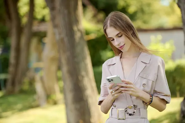 Eine junge Frau mit Magersucht genießt ihre Zeit draußen, inmitten der Schönheit der Natur mit ihrem Handy — Stockfoto