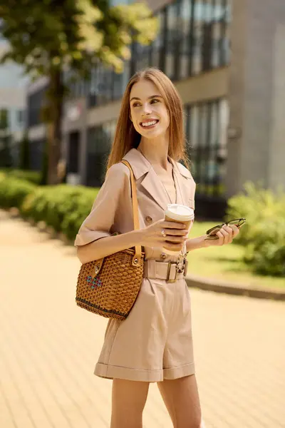 A young woman with a joyful expression walks through a sunlit area, enjoying coffee and nature. — Stock Photo