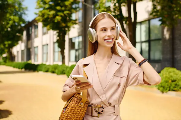 A young woman with anorexia relishes a bright day outside, smiling and listening to music with headphones while walking. — Stock Photo
