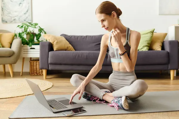 A young woman with anorexia exercises in her living room, focused on her workout routine while using a laptop. — Stock Photo