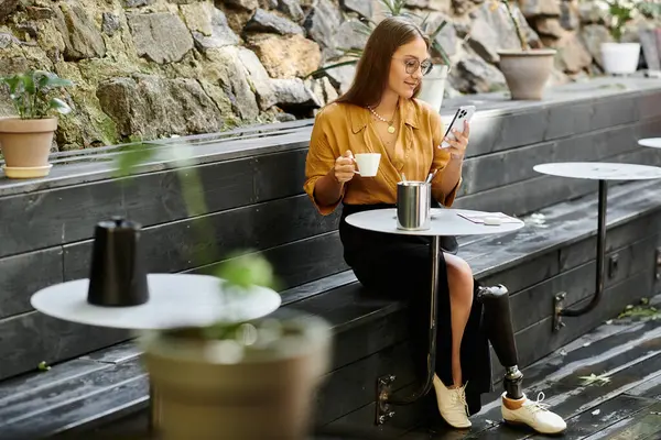 Sipping coffee while using her phone, a young woman with a prosthetic leg enjoys her time in a charming cafe setting. — Stock Photo