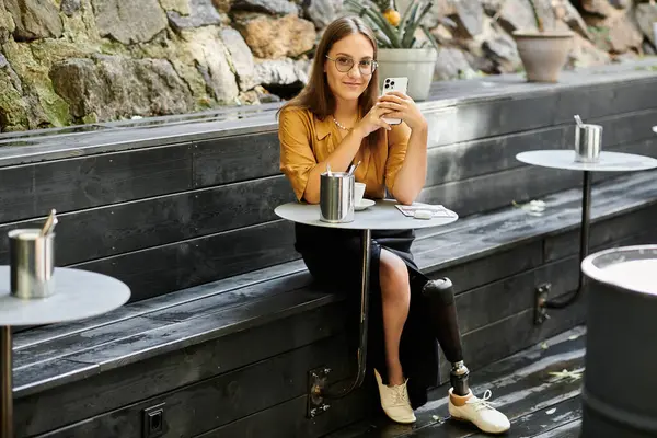 In a cozy cafe, a young woman smiles while using her phone, embracing her vibrant lifestyle with a prosthetic leg. — Stock Photo